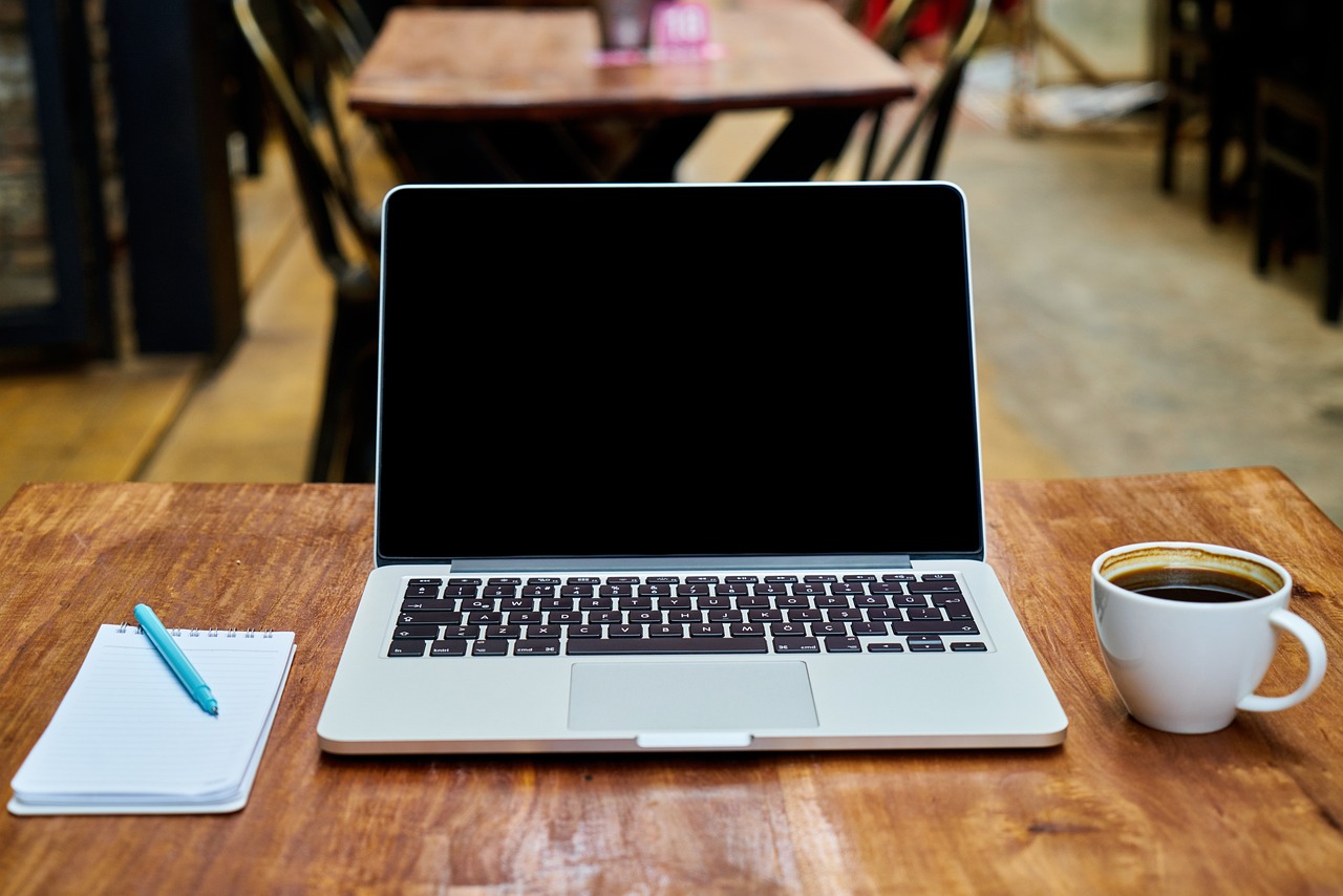 Holztisch mit Laptop, Notizbuch und Kaffeetasse